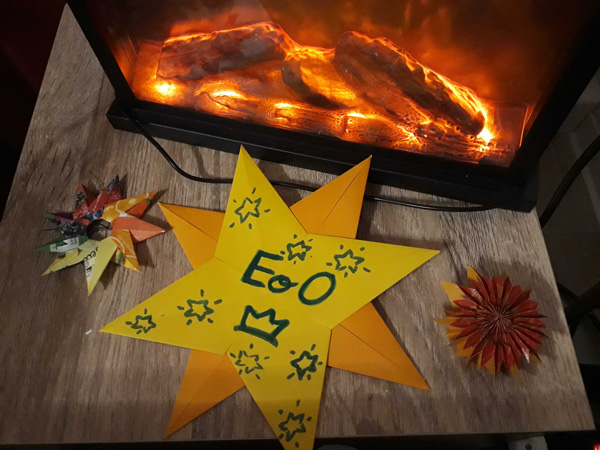 Gelber Papierstern mit dem Empire-Logo, auf einem Tisch vor einem Kaminfeuer