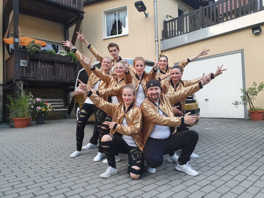 Neun Tänzerinnen des Empires posieren zusammen in goldenen Kostümen vor einem Auftritt