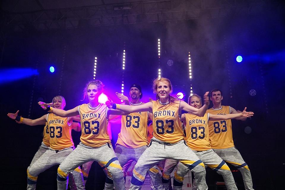 Aufführung der Hip Hop Show auf dem Stadtfest Dresden in Hip Hop Kostümen, Tänzer bilden Gruppe mit geöffneten Armen, lilanes Bühnenlicht von hinten